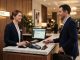 Female hotel receptionist greeting a male guest warmly at check-in.