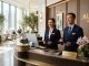 A male and female front desk receptionist smiling warmly at guests in a hotel lobby.